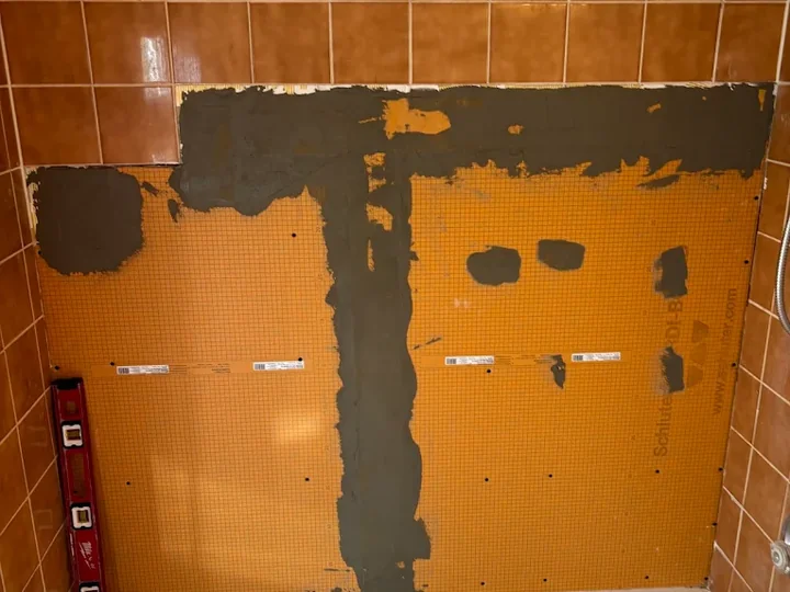 Bathroom wall repair with orange backing panels above a bathtub before tiling