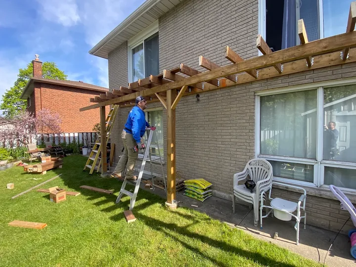 Worker building a timber deck frame beside a brick house