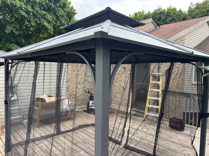 Assembled metal gazebo with a roof and mesh side panels on a deck